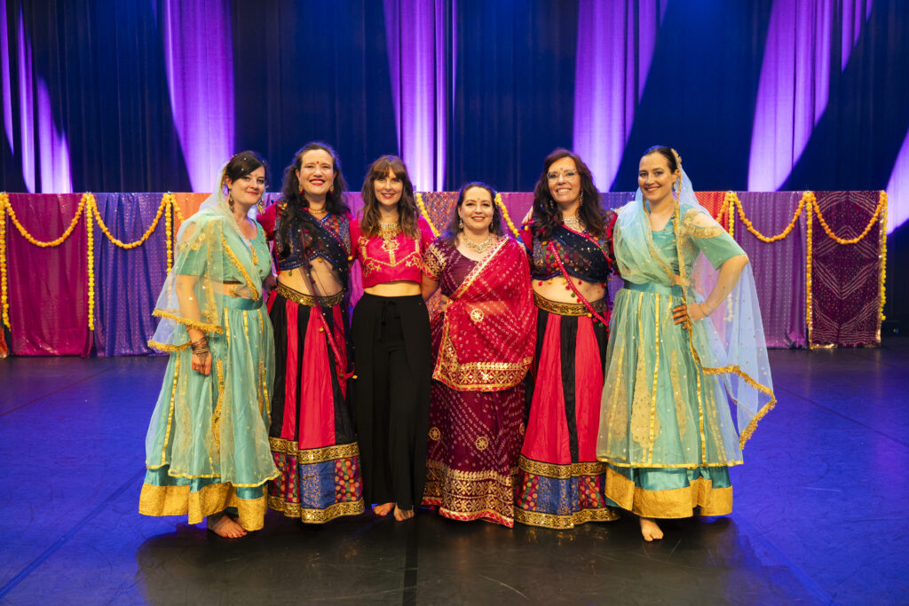 6 femmes en habits colorés de style indien / bollywood posent sur une scène de spectacle.